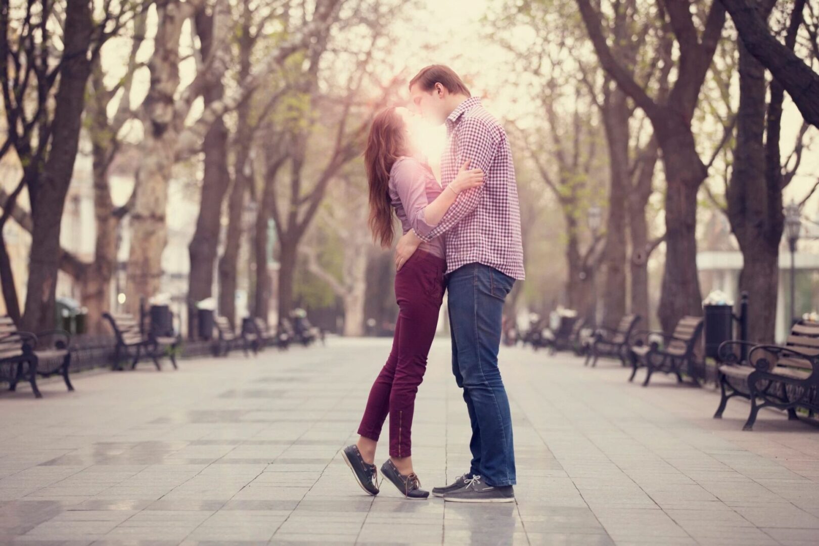 A man and woman kissing on the sidewalk.